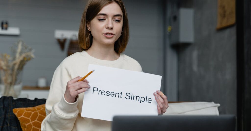 Young woman teaches English grammar online, holding a 'Present Simple' note and pencil.